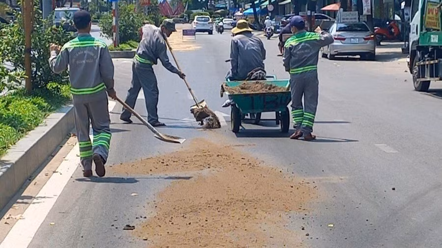 Nhân viên công ty môi trường rải cát xử lý vết dầu nhớt phủ trên nền đường.