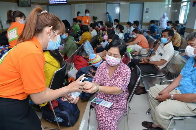 Nhân viên BV hướng dẫn và xịt dung dịch rửa tay cho người nhà bệnh nhân đến khám tại BV ĐH Y Dược TP.HCM