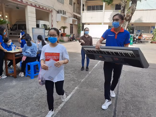 Thí sinh mang theo nhạc cụ để dự thi năng khiếu âm nhạc được các tình nguyện viên hỗ trợ.