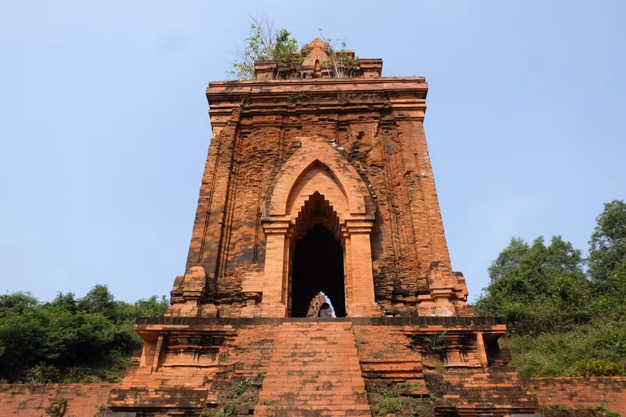 Vòm cửa chính giống hình mũi lao có nhiều lớp liên tiếp vút lên cao, hai mặt còn lại là cửa giả có kích thước và vòm được mô phỏng giống cửa thật. Quanh chân tháp có những rãnh dọc được soi lõm, tạo thành những cột ốp có dáng cao vút, thanh thoát nhẹ nhàng. Ảnh: Hoàng Vinh.