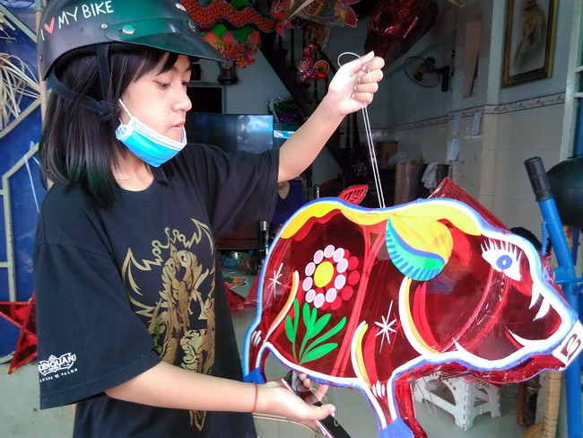 Một học sinh đến chọn mua mẫu lồng đèn hình chú heo Đông Hồ rất đẹp mắt để về vui Trung thu tại trường. Đây là mẫu mới cho mùa Trung thu năm nay do cơ sở của gia đình anh Bình sản xuất.