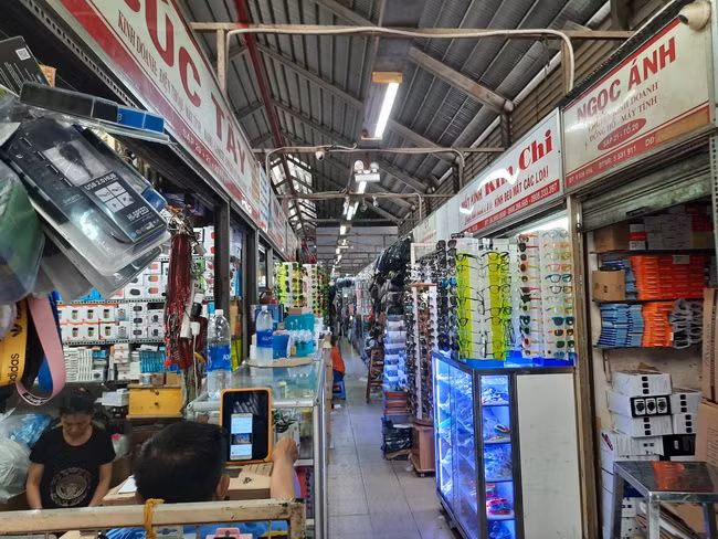 Lối vào bên trong chợ nhỏ hẹp là các gian hàng kinh doanh đồ điện tử, đồng hồ..