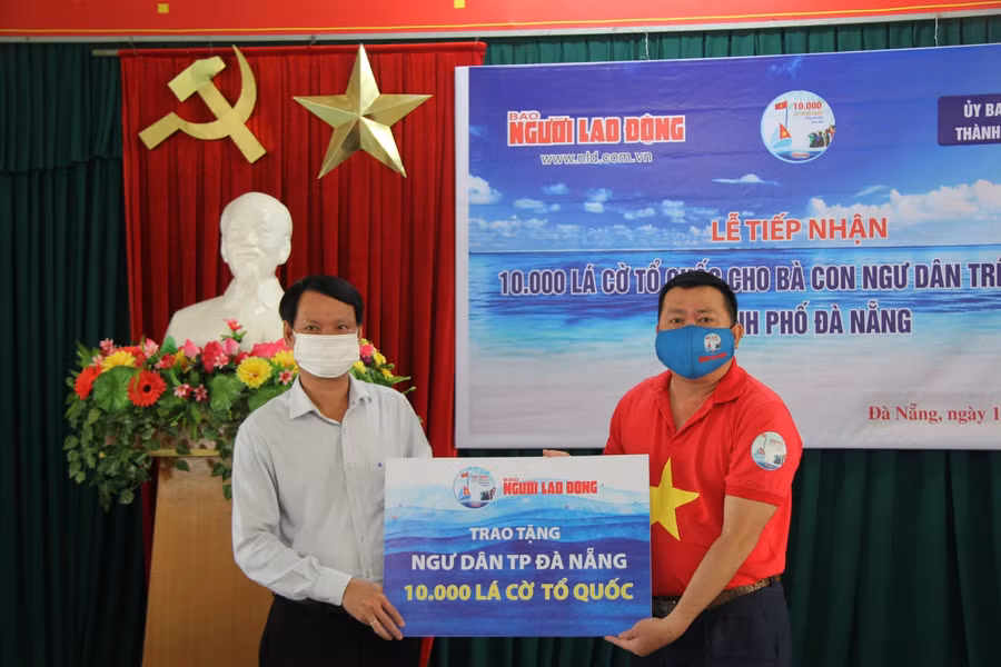 Nhà báo Đặng Hoàng Dũng (bên phải) - Trưởng Văn phòng Đại diện Báo Người Lao động khu vực miền Trung, trao tượng trưng 10.000 lá cờ Tổ quốc cho ngư dân.