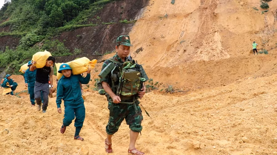 Bộ đội, dân quân tự vệ mang nhu yếu phẩm vượt qua những điểm sạt lở để hỗ trợ Nhân dân.