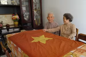 Bà Nguyễn Thị Ngọc Lan cùng chồng - ông Nguyễn Du (lúc còn sống) bên kỷ vật là lá cờ Tổ quốc do chính tay bà may. Ảnh: TT -HG