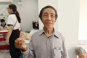 Ông Lương Văn Nông nhận quà tặng 200.000 đồng cho 2 vợ chồng ông từ điểm chi trả của UBND phường Bến Thành. Ảnh: Phúc Uyên.