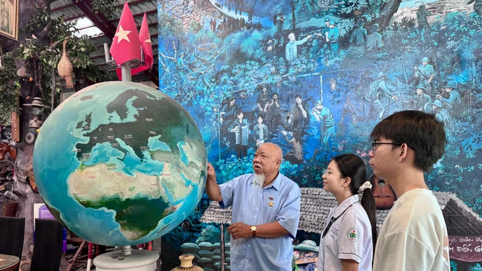 Cựu chiến binh Lâm Xuân Quang cùng học sinh tham quan quả địa cầu, tái hiện hành trình ra đi tìm đường cứu nước của Bác Hồ. Ảnh: Thùy Linh