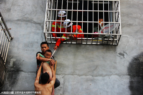 Em bé được hàng xóm đỡ xuống sau khi lực lượng cứu hỗ giải thoát được phần đầu bị kẹt. Ảnh: News Sina. be-trai-ket-dau-vao-chuong-cop-chung-cu-khi-o-nha-mot-minh-2