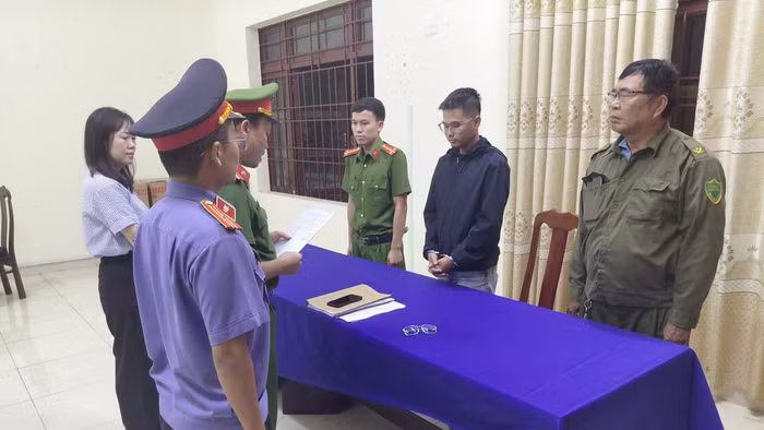 Công an tống đạt các Quyết định khởi tố vụ án, khởi tố bị can và Lệnh bắt tạm giam đối với Võ Nguyễn Duy An (áo đen). Ảnh: Công an cung cấp
