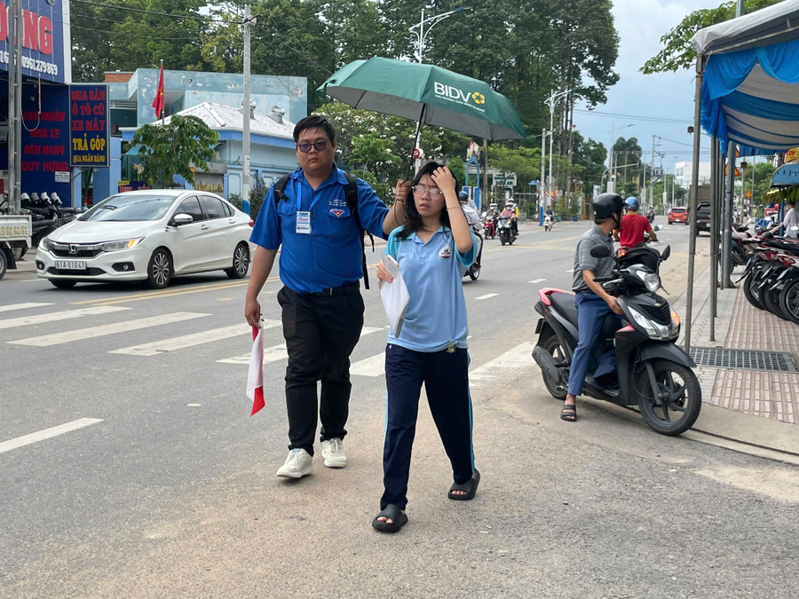 Học sinh được tình nguyện viên che ô tại điểm thi trường THPT Nguyễn Trãi. (Ảnh: Hà An). ghi-nhan-lam-thu-tuc-binh-duong-1.jpg