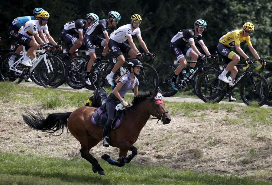 Một phụ nữ trẻ cưỡi ngựa bên cạnh đội đua xe đạp tham gia Tour de France lần thứ 104