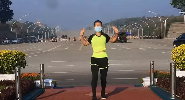 Người phụ nữ tập aerobics khi xe quân sự chạy sau lưng.