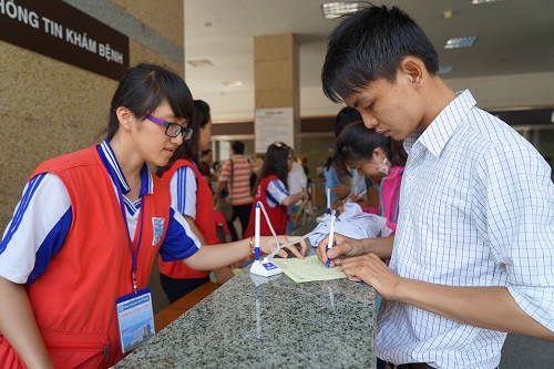 Hồng Gấm (sinh viên Khoa Điều dưỡng - Kỹ thuật Y học) đang hướng dẫn người nhà bệnh nhân làm thủ tục khám bệnh. Ảnh: Thi Ngoan.
