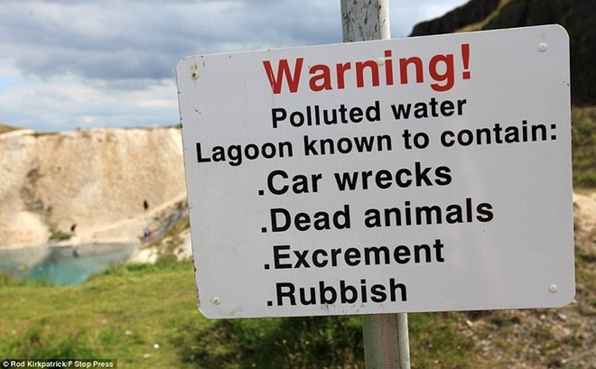 Một tấm biển với nội dung cảnh báo rằng nước trong hồ ô nhiễm nặng và chứa xác ô tô, động vật chết, phân và rác. ga