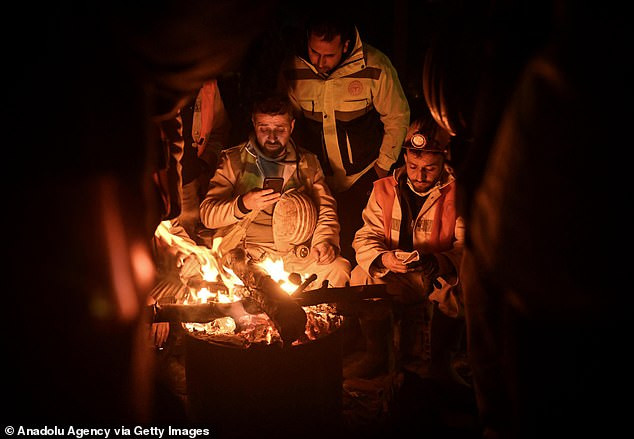 Thợ mỏ Sinan Durdu (giữa) sưởi ấm quanh ngọn lửa ở Adiyaman. Anh đã kéo một cô gái 17 tuổi còn sống ra khỏi đống đổ nát sau khi xuống tới độ sâu 8 mét. Thợ mỏ Sinan Durdu (giữa) sưởi ấm quanh ngọn lửa ở Adiyaman. Anh đã kéo một cô gái 17 tuổi còn sống ra khỏi đống đổ nát sau khi xuống tới độ sâu 8 mét.