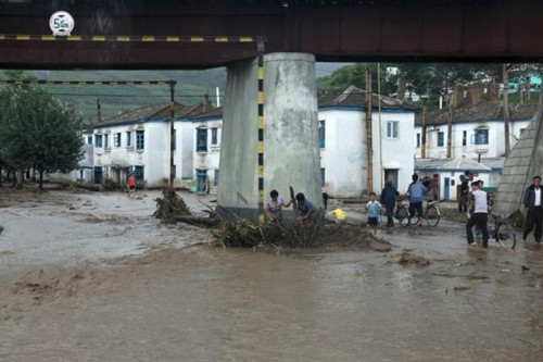 Người dân dọn rác trong nước lũ dưới cầu Rason, Triều Tiên hôm 22-8 (Ảnh: Reuters)