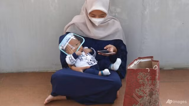 Một phụ nữ Indonesia đang bế em bé đeo tấm chắn phòng dịch.