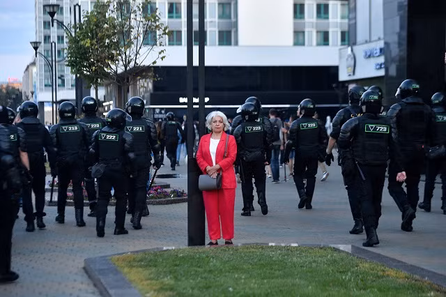 Một phụ nữ đứng bên cột đèn ở thủ đô Minsk của Belarus khi cảnh sát chống bạo động di chuyển dọc đường phố trong cuộc biểu tình của những người ủng hộ phe đối lập, cáo buộc Tổng thống Alexander Lukashenko gian lận bầu cử. [Sergei Gapon / AFP]