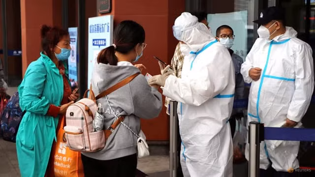 Nhân viên mặc đồ bảo hộ kiểm tra bằng chứng về kết quả xét nghiệm Covid-19 âm tính đối với du khách tại lối vào Ga xe lửa Tây Cáp Nhĩ Tân, Trung Quốc.