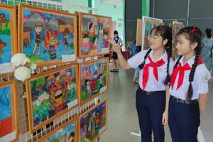 Hai em học sinh đang ngắm các bức vẽ của các thí sinh tham gia hội thi vẽ tranh "Em vẽ sắc màu quê hương". Ảnh: Nhà thiếu nhi Bình Dương
