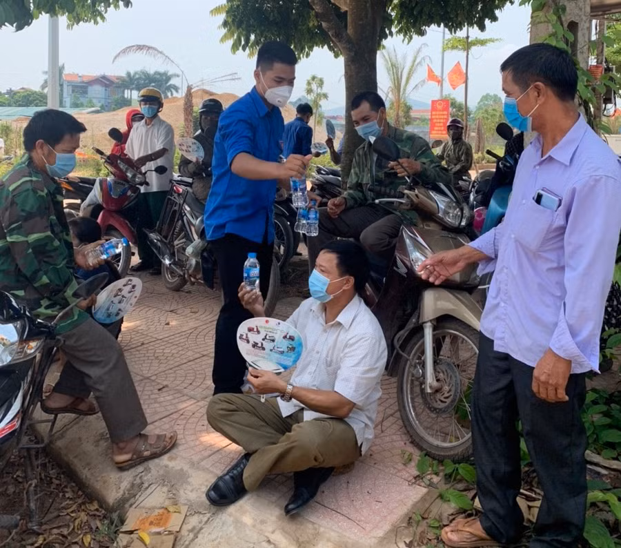 Sau khi tặng nước cho phụ huynh, thanh niên tình nguyện tuyên truyền phụ huynh di chuyển không tụ tập đông người để phòng dịch Covid-19.