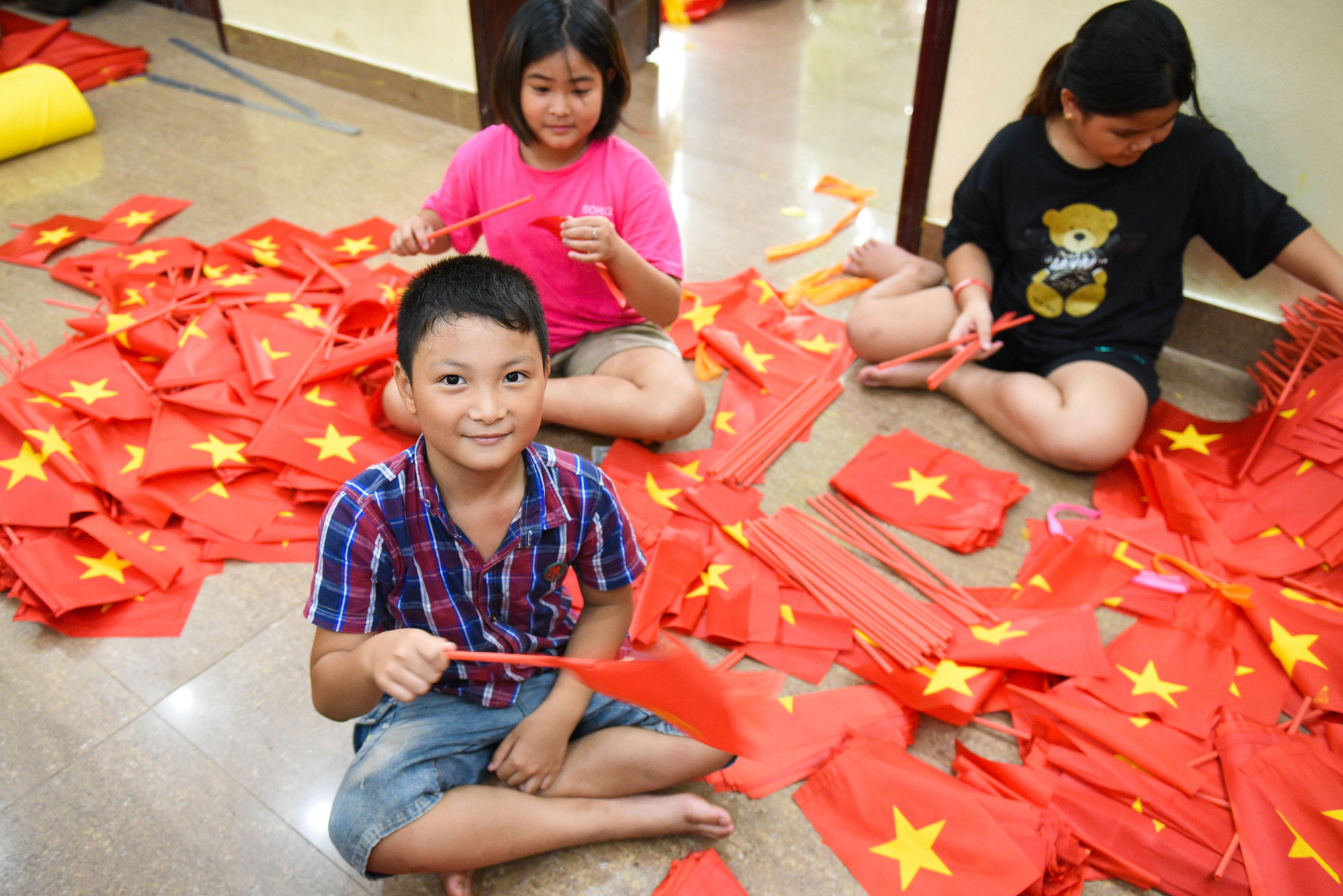 Nhiều em nhỏ tham gia lắp những lá cờ Tổ quốc cầm tay (cờ Tổ quốc nhỏ - loại cầm tay cho học sinh vào năm học mới).