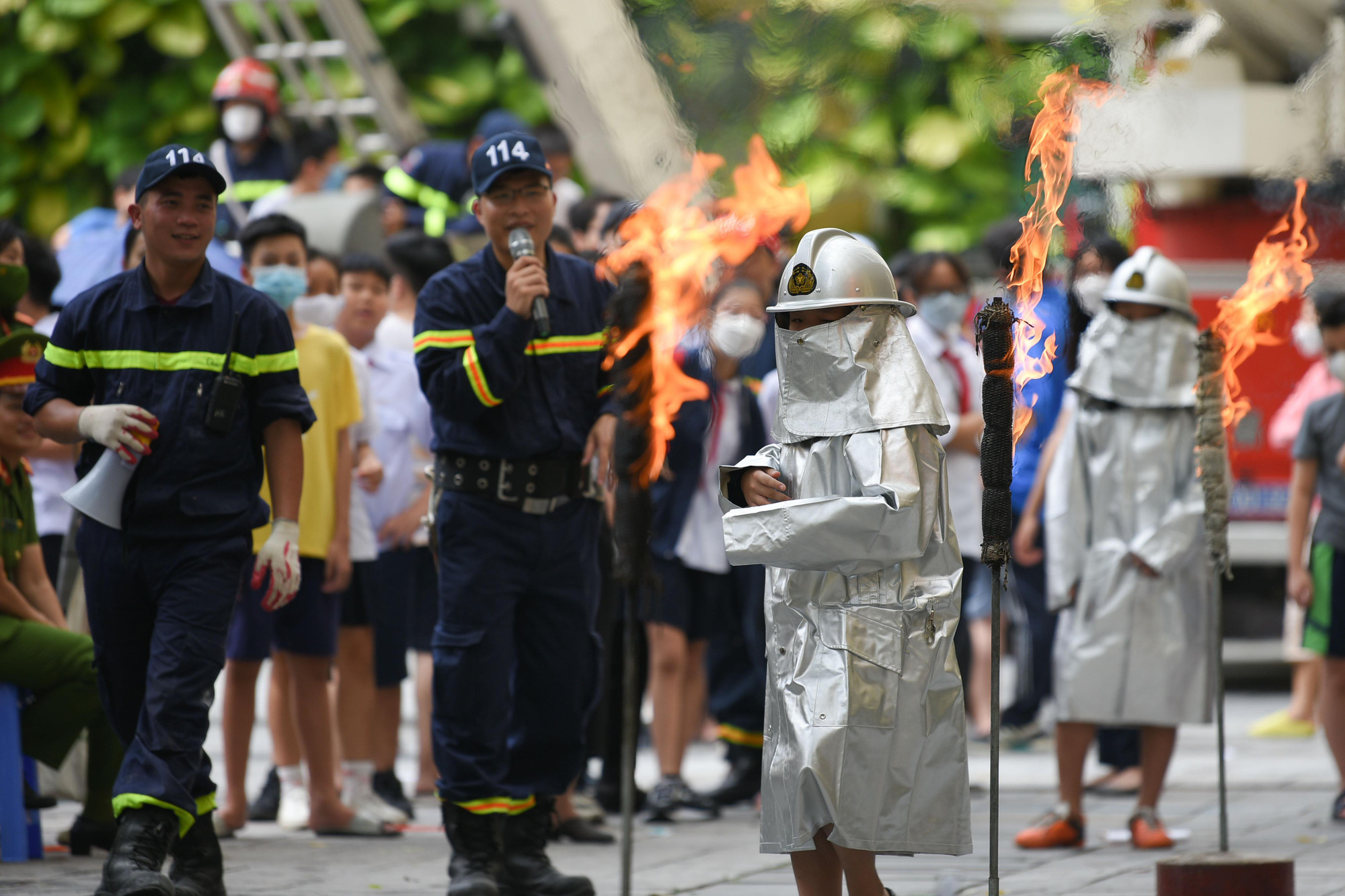 Các em học sinh mặc trang phụ chữa cháy chuyên dụng chạy qua các ngọn lửa.