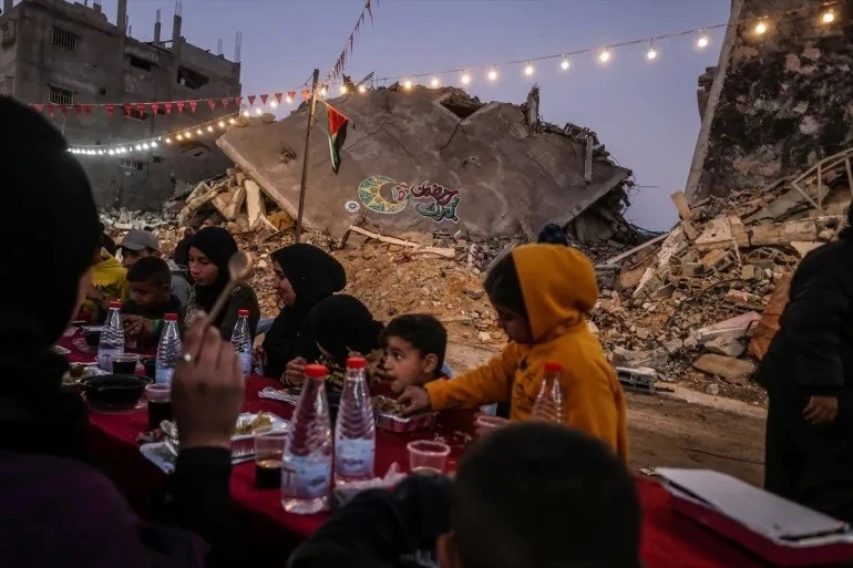 Các gia đình dùng bữa Iftar trong ngày đầu tiên của tháng lễ Ramadan giữa những tòa nhà bị phá hủy bởi cuộc ném bom của Israel [Ảnh: Ali Jadallah/Anadolu]