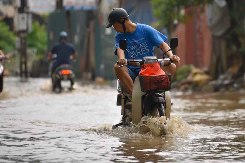 Người dân Hà Nội co chân trên xe máy lội qua đường ngập dù trời không mưa