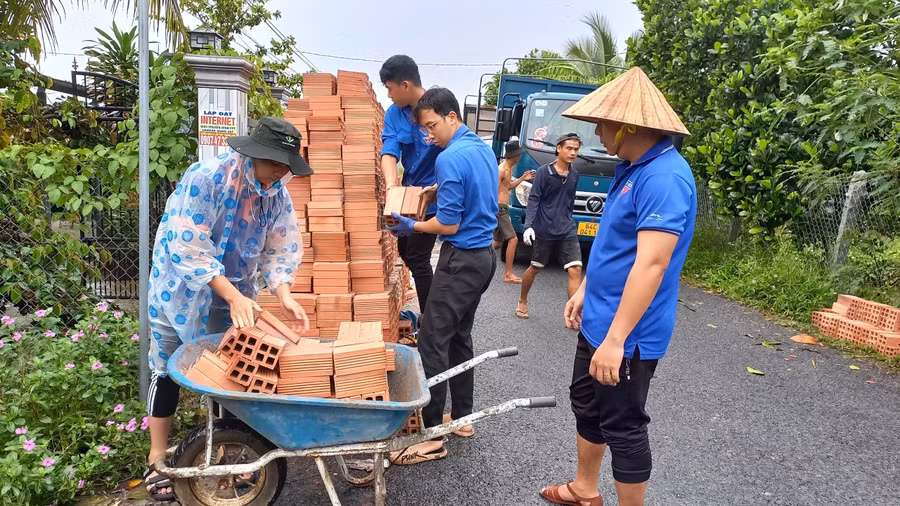 Sinh viên trường Đại học sư phạm kỹ thuật Vĩnh Long cùng với đoàn viên thanh niên hỗ trợ vận chuyển vật tư giúp gia đình em Nhi trong buổi lễ khởi công nhà.