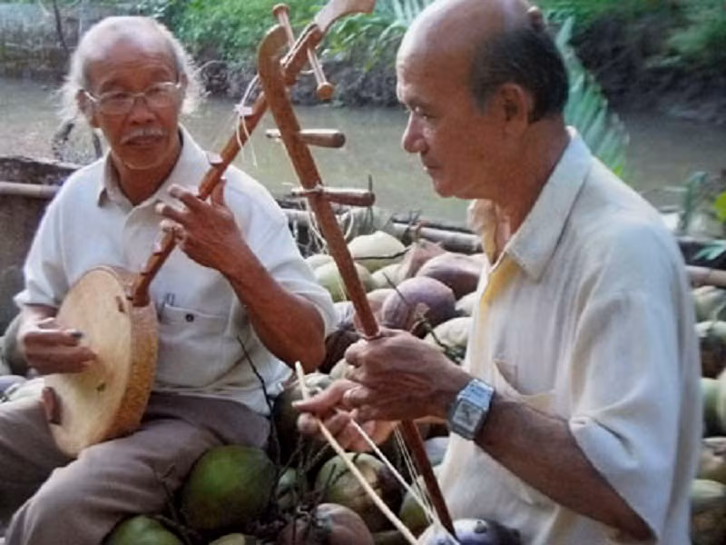 Nhạc sĩ Lê Dân (trái) và nhạc sĩ - nghệ nhân Võ Văn Bá đang so đàn, diễn tấu bằng nhạc cụ làm từ gỗ dừa
