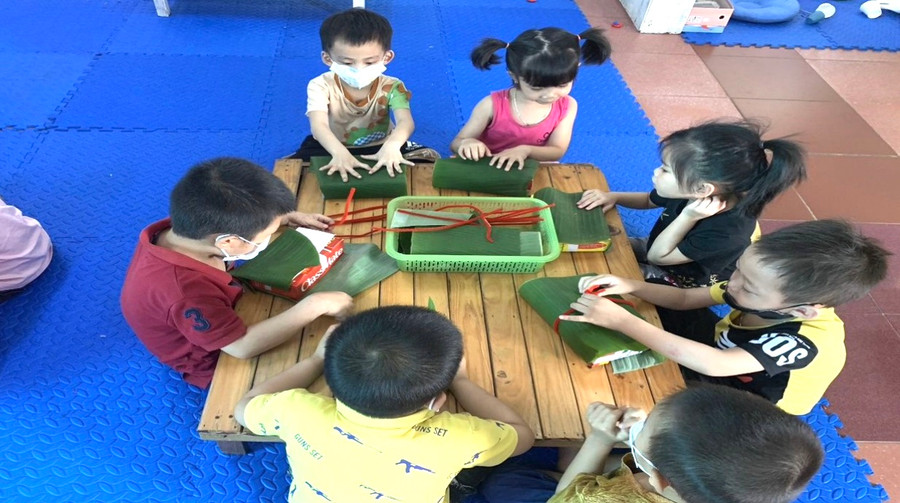 Học sinh mầm non tập gói bánh chưng.