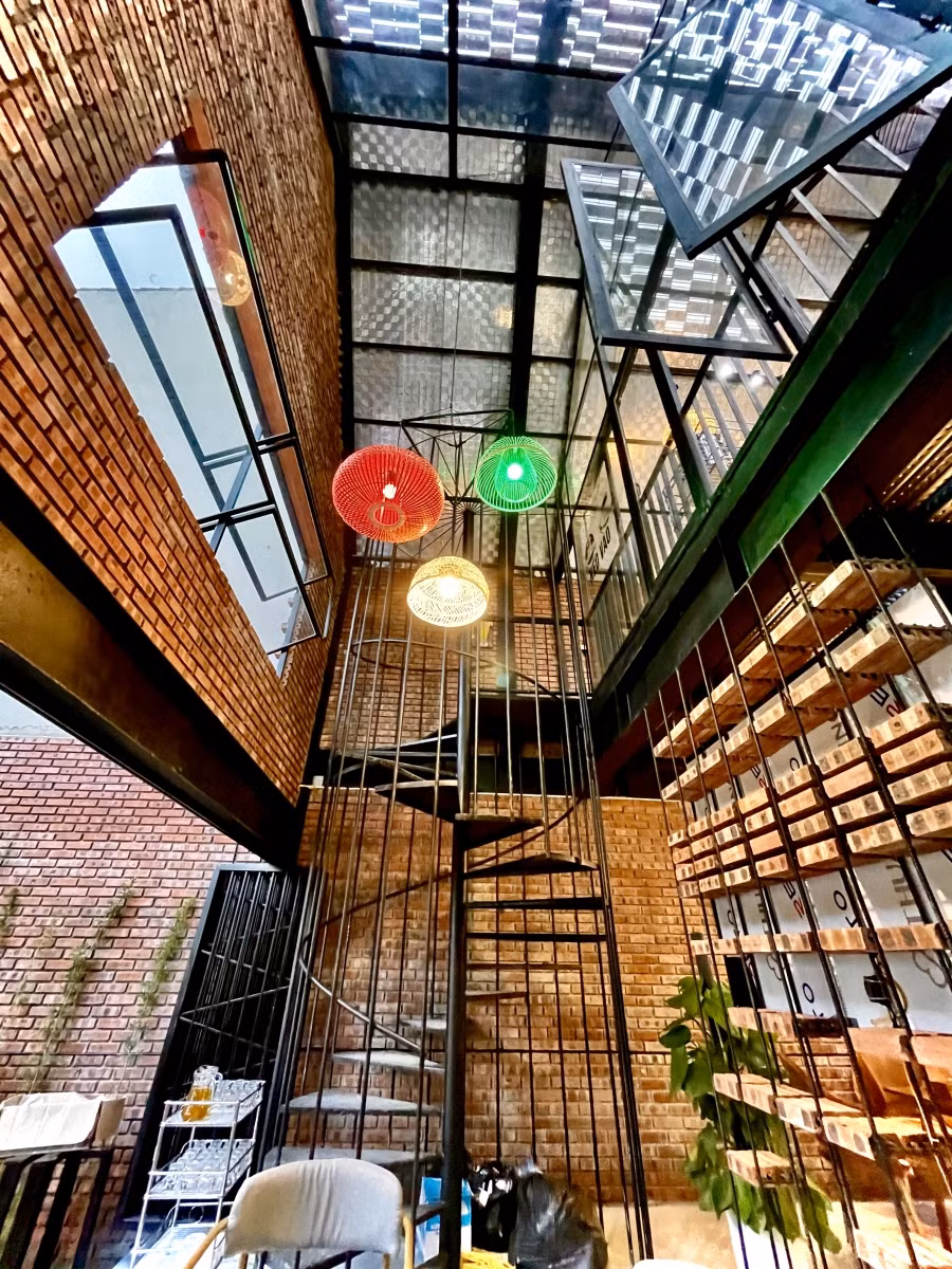 Phần cầu thang đơn giản nhưng gây ấn tượng bởi thiết kế hình xoáy ốc bằng thép chịu lực tiền chế. Nhìn tổng thể chiếc cầu thang như một lồng chim lớn đặt giữa trung tâm quán