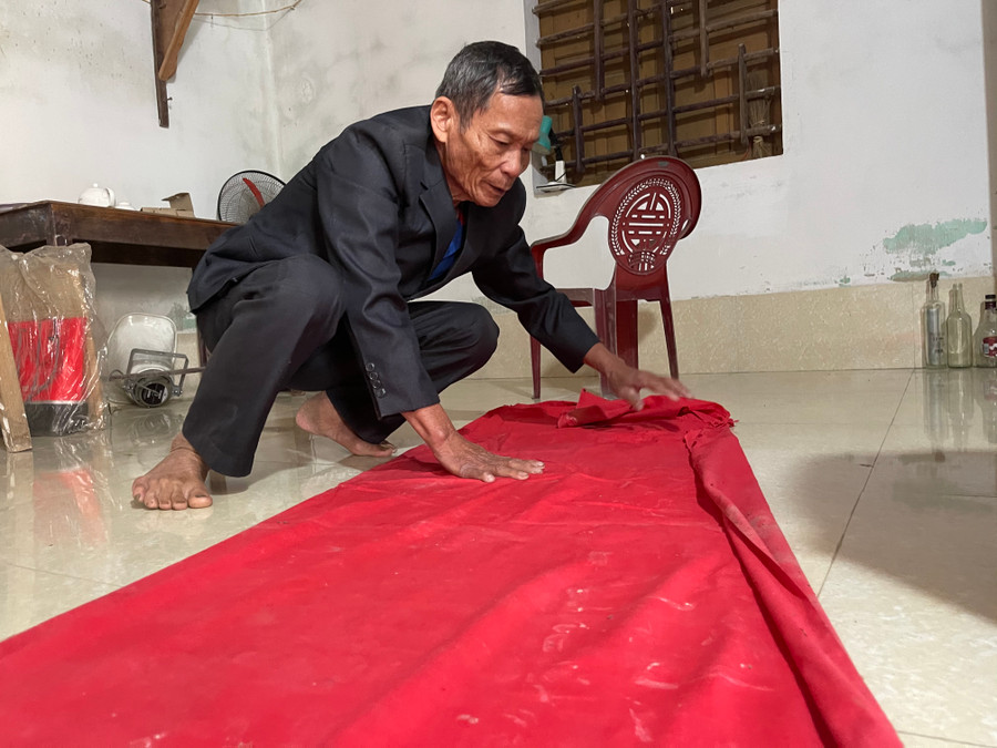 Sau khi đặt một tấm vải đỏ quanh nền nhà, ông Tân mới chầm chậm trải nhẹ sắc phong ra nền nhà để mọi người chiêm ngưỡng.