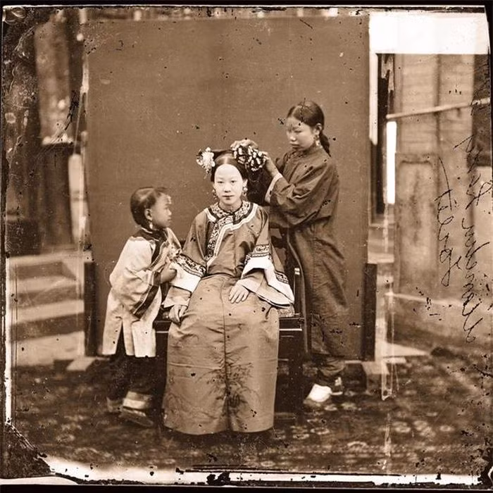 Một người phụ nữ quý tộc người Mãn đang được gia nô chỉnh sửa mái tóc.