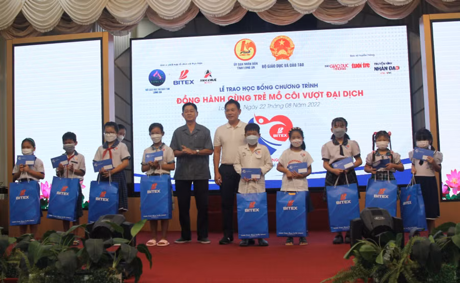 Ông Đỗ Quang Vinh thành viên Hội đồng quản trị (áo trắng), Tổng Giám đốc Công ty Cổ phần Anh Khuê Watch và ông Võ Lê Tuấn, Chủ tịch hội khuyến học tỉnh Long An tặng học bổng cho các em học sinh.