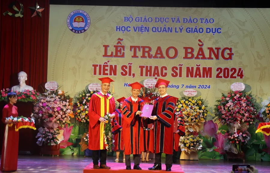 PGS.TS Phạm Văn Thuần (ngoài cùng bên phải) và PGS.TS Trần Hữu Hoan - Phó Giám đốc Học viện Quản lý giáo dục trao bằng tiến sĩ, tặng hoa chúc mừng học viên.