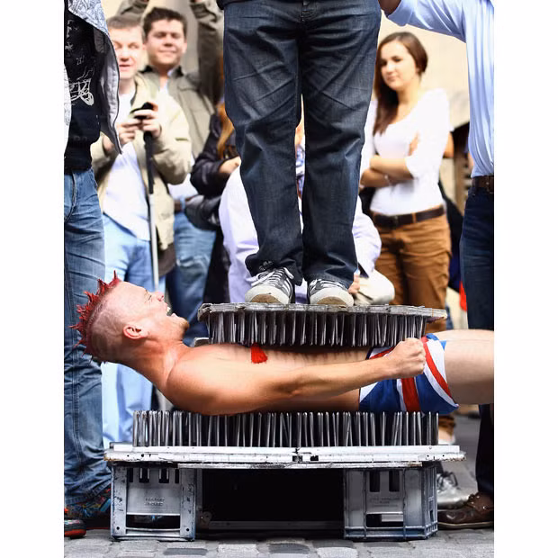 A street entertainer lays down on a bed of nails during a performance on the Royal Mile during the Edinburgh Fringe Festival 