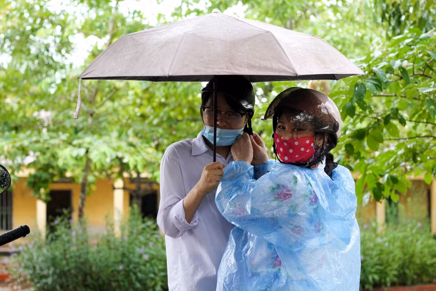 Phụ huynh cẩn thận giúp con cài mũ bảo hiểm dưới cơn mưa.