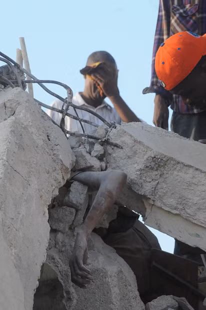 A man covers his face behind a person trapped in the rubble of a collapsed building in Port-au-Prince