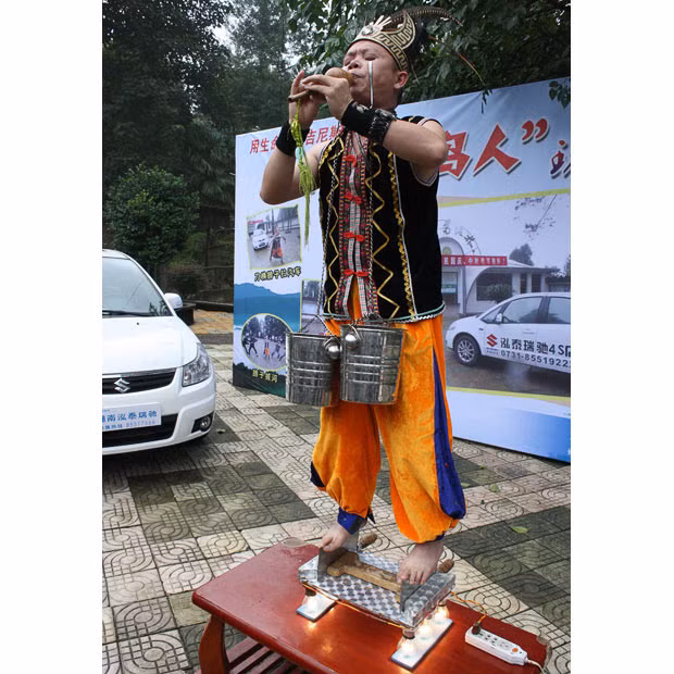 Những hình ảnh ấn tượng trong tuần ảnh 12 A stunt man who performs multiple tricks at once has been wowing the crowds at a park in Changsha, Hunan Province, China. Yang Guanghe, 37, isn’t content with performing just one hair-raising stunt - he likes to carry out several from his 30-strong repertoire all at once. For example, during one performance Yang put four lit light bulbs on a table before placing a board on top. On this board were two sharp knives with their blades facing up, which Yang stood on in bare feet. He then attached two hooks onto his lower eyelids from which hung two buckets of water. To round off the trick Yang then began to play a flute...