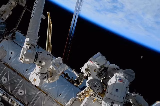 Phi hành gia NASA Stephen Bowen (phải) và phi hành gia UAE Sultan AlNeyadi làm việc trên một cụm ăng-ten bên ngoài Trạm Vũ trụ Quốc tế với Trái đất và mặt trăng lơ lửng trên đầu. Ảnh: NASA TV