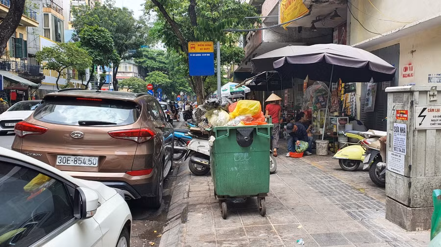 Nhiều người dân đứng đợi xe buýt đang phải chịu mùi từ những xe rác được đặt ở ví trí ngay bên cạnh điểm, nhà chờ.