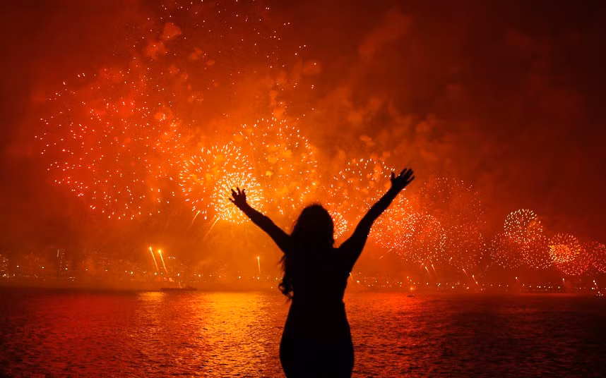 A woman celebrates the New Year as she watches fireworks exploding above Copacabana beach in Rio de Janeiro