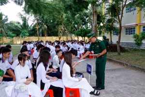 Cán bộ đồn Biên phòng Trung Bình phát tờ rơi tuyên truyền cho các em học sinh.