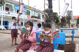 Các em đọc sách ở tủ sách di động dưới tán cây trong sân trường.