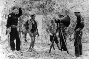 Binh lính Nhật Bản và cảnh sát Philippines đứng cạnh loa phóng thanh cung cấp thông tin về gia đình các binh sĩ Nhật Bản, Lubang, Philippines, năm 1959.