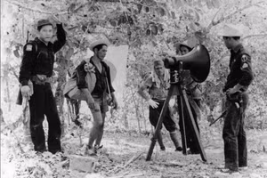 Binh lính Nhật Bản và cảnh sát Philippines đứng cạnh loa phóng thanh cung cấp thông tin về gia đình các binh sĩ Nhật Bản, Lubang, Philippines, năm 1959.