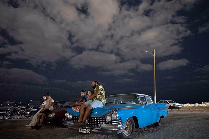 Một gia đình xem chiếu phim ngoài trời ở Havana, tháng 4/2024. (Ảnh: REUTERS/Alexandre Meneghini) Chùm ảnh những chiếc xe cổ tuyệt đẹp trên đường phố Havana