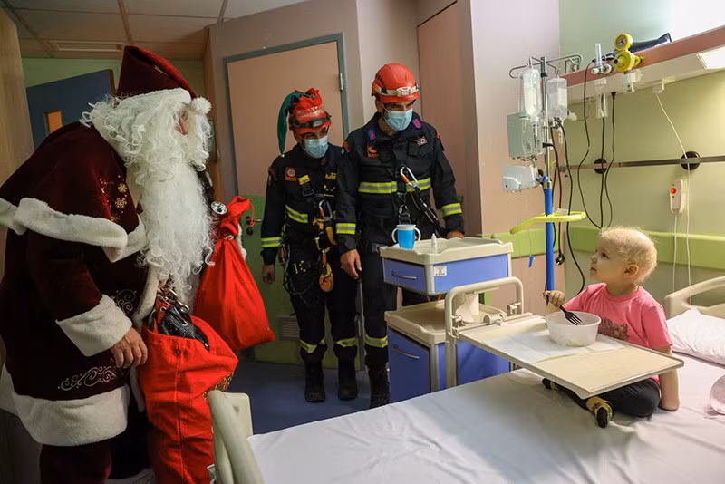 Một lính cứu hỏa Hy Lạp, hóa trang thành Ông già Noel, đến thăm một bệnh nhi của khoa Ung bướu “Marianna V. Vardinoyiannis” thuộc Bệnh viện Nhi Aghia Sofia ở Athens, Hy Lạp. Ảnh: REUTERS/Stelios Misinas ong-gia-noel-den-roi-day-2024-07.jpg